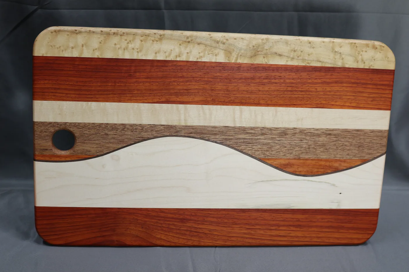 Curved handmade charcuterie board with contrasting hardwood stripes